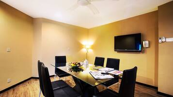 A conference room with a glass table, black chairs, a ceiling fan, a TV, and a telephone.