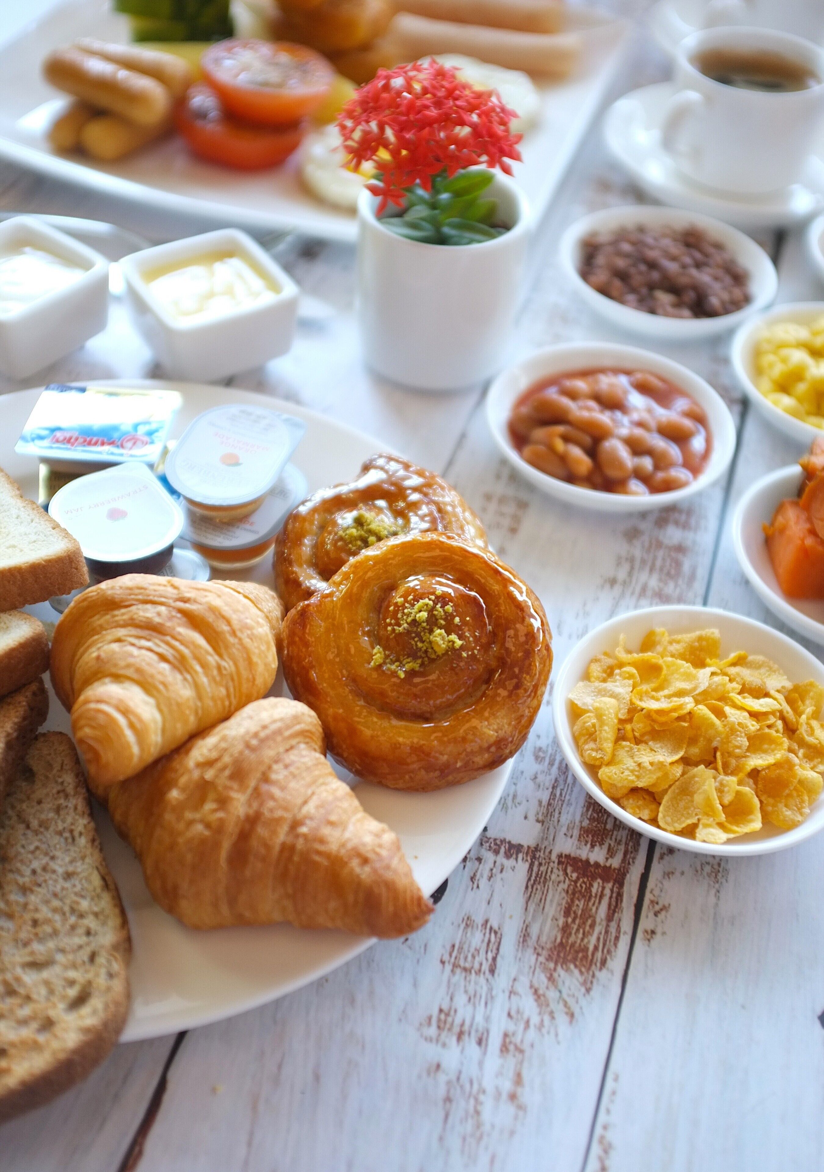 Un assortiment de viennoiseries, de pain et de diverses garnitures disposé sur une table en bois pour le petit-déjeuner.