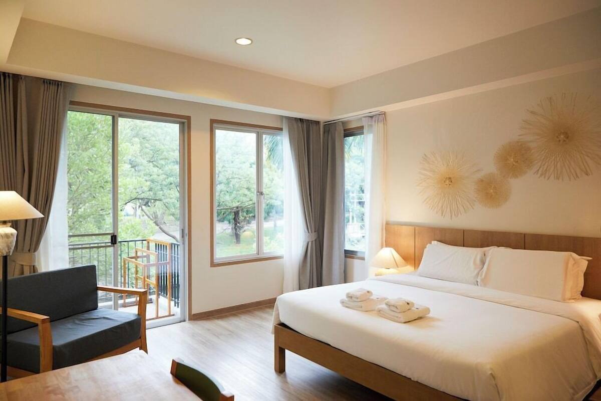 Ein Hotelzimmer mit Bett, Stuhl, Tisch und großen Fenstern mit Vorhängen.