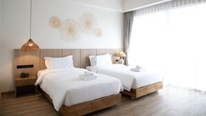 A hotel room with two beds, a hanging light fixture, a wall decoration, a nightstand, and a window with curtains. - The Leela Resort & Spa Pattaya (Pattaya)