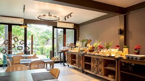 A modern dining area with a buffet setup, wicker furniture, and large windows offering a view of greenery. - The Leela Resort & Spa Pattaya (Pattaya)