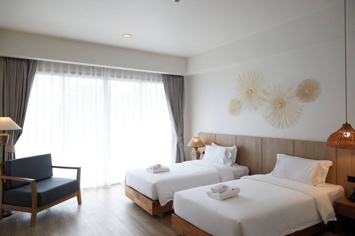 Ein Hotelzimmer mit zwei Betten, einem Sessel, einer Lampe und einem Wandbild.