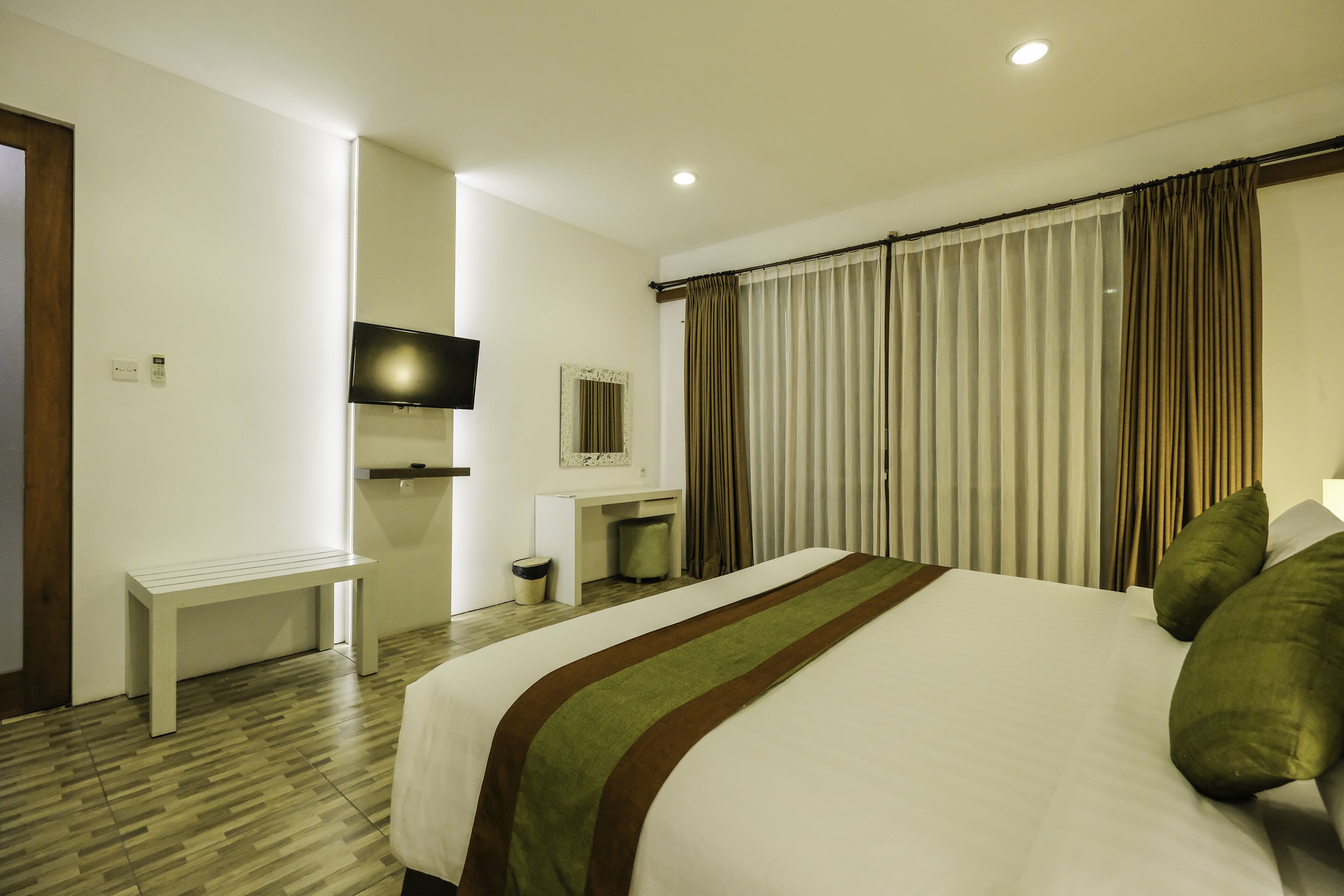 A hotel room with a large bed, a desk, a television, and a window with curtains.