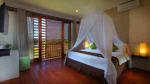 Un dormitorio con cama con dosel, un reposapiés verde, una mesita de noche con lámpara y vistas a través de una puerta corredera.