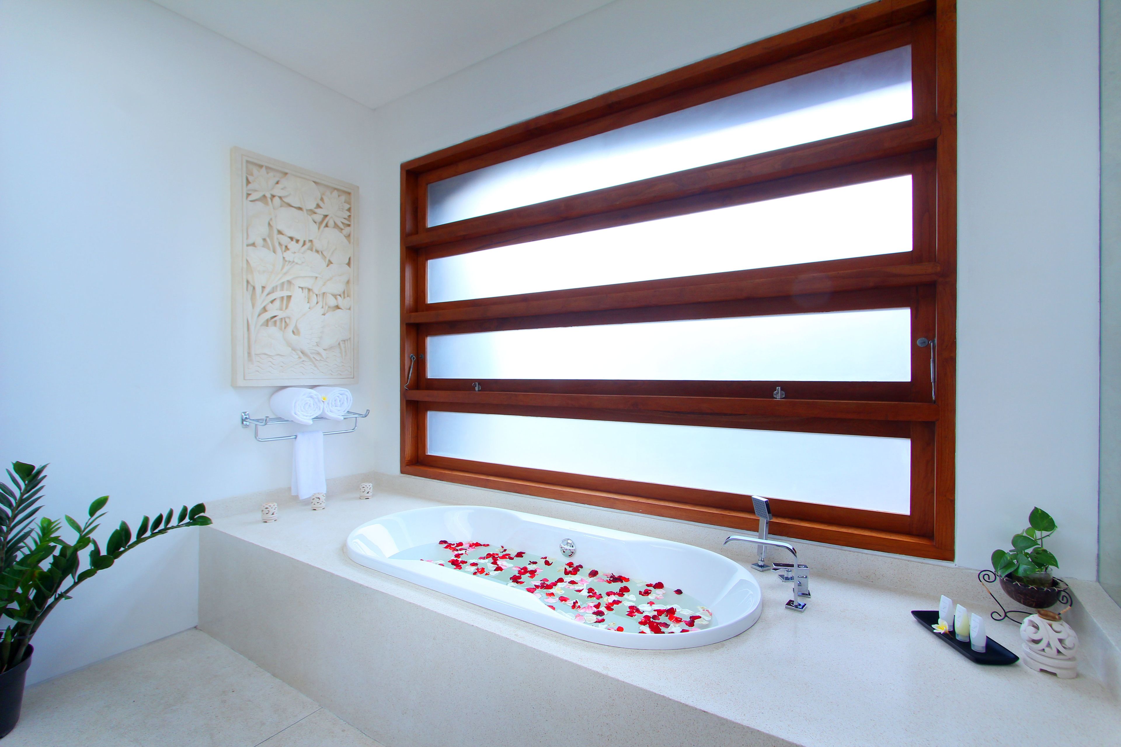 Un baño moderno con una bañera independiente, un ventanal de madera y una planta en maceta.