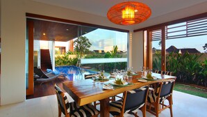Un comedor con una mesa de madera dispuesta para seis personas, rodeada de sillas a rayas de cebra, y vistas a una piscina y vegetación exuberante.