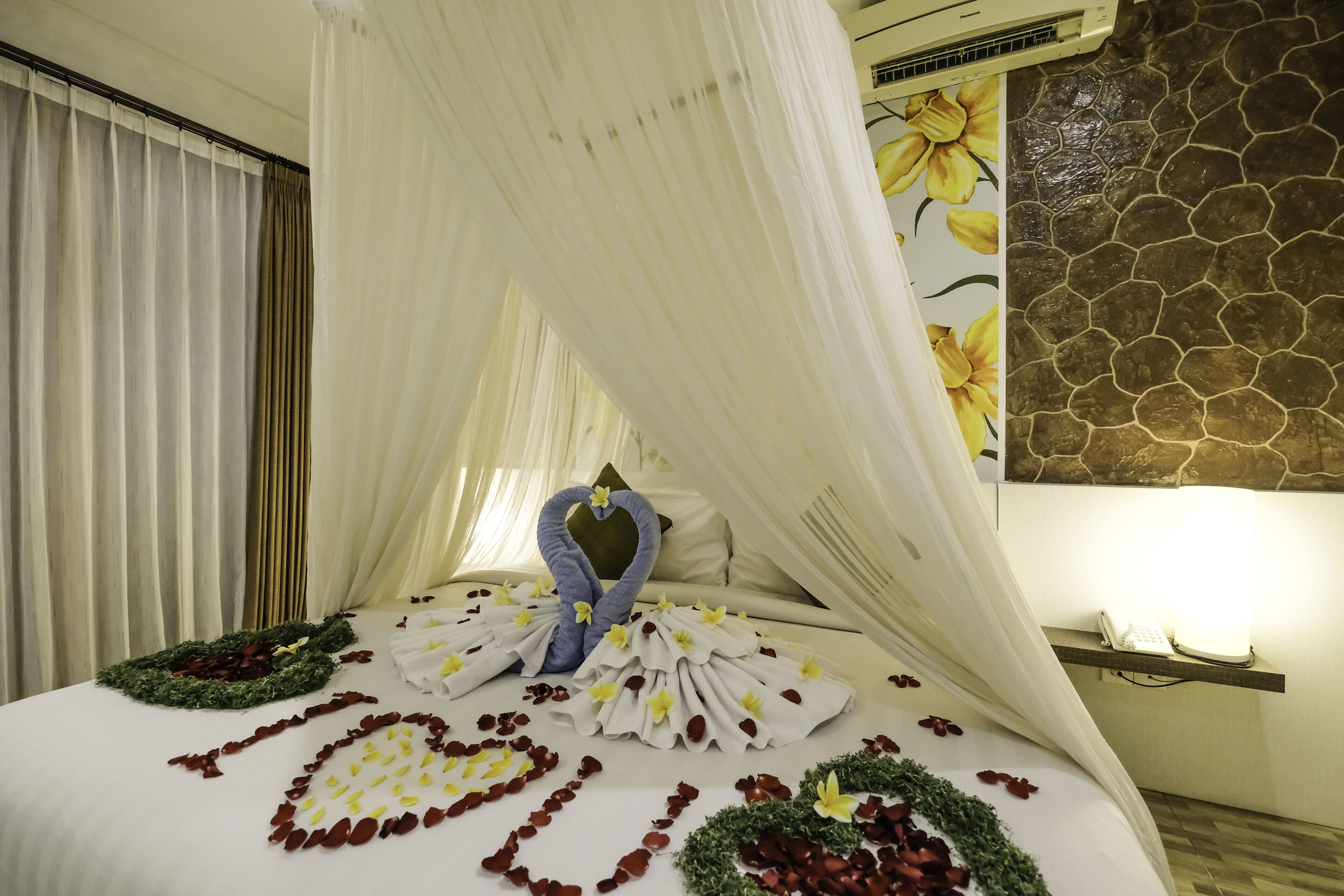 Une chambre d’hôtel avec un lit agrémenté de compositions florales et de décorations en forme de cœur, un baldaquin et un mur en pierre.