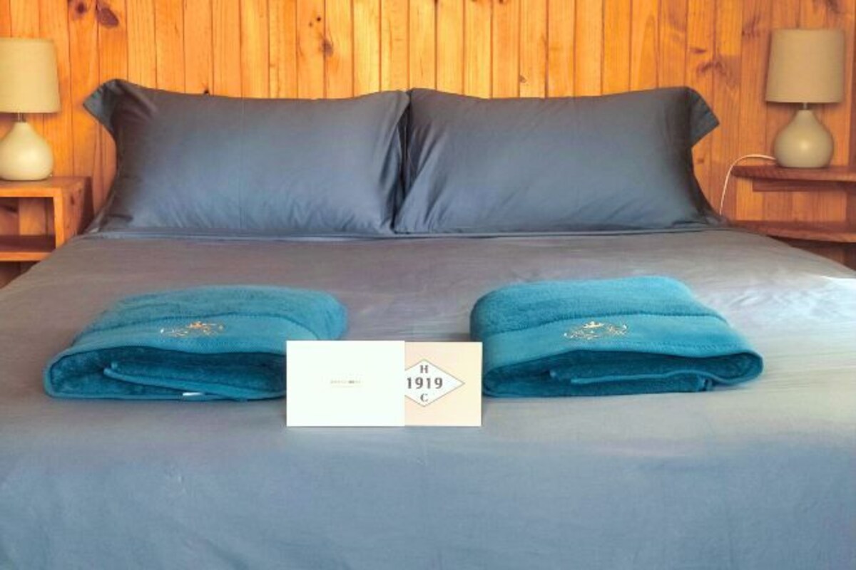 A neatly made bed with dark blue linens and two folded towels on the bed.