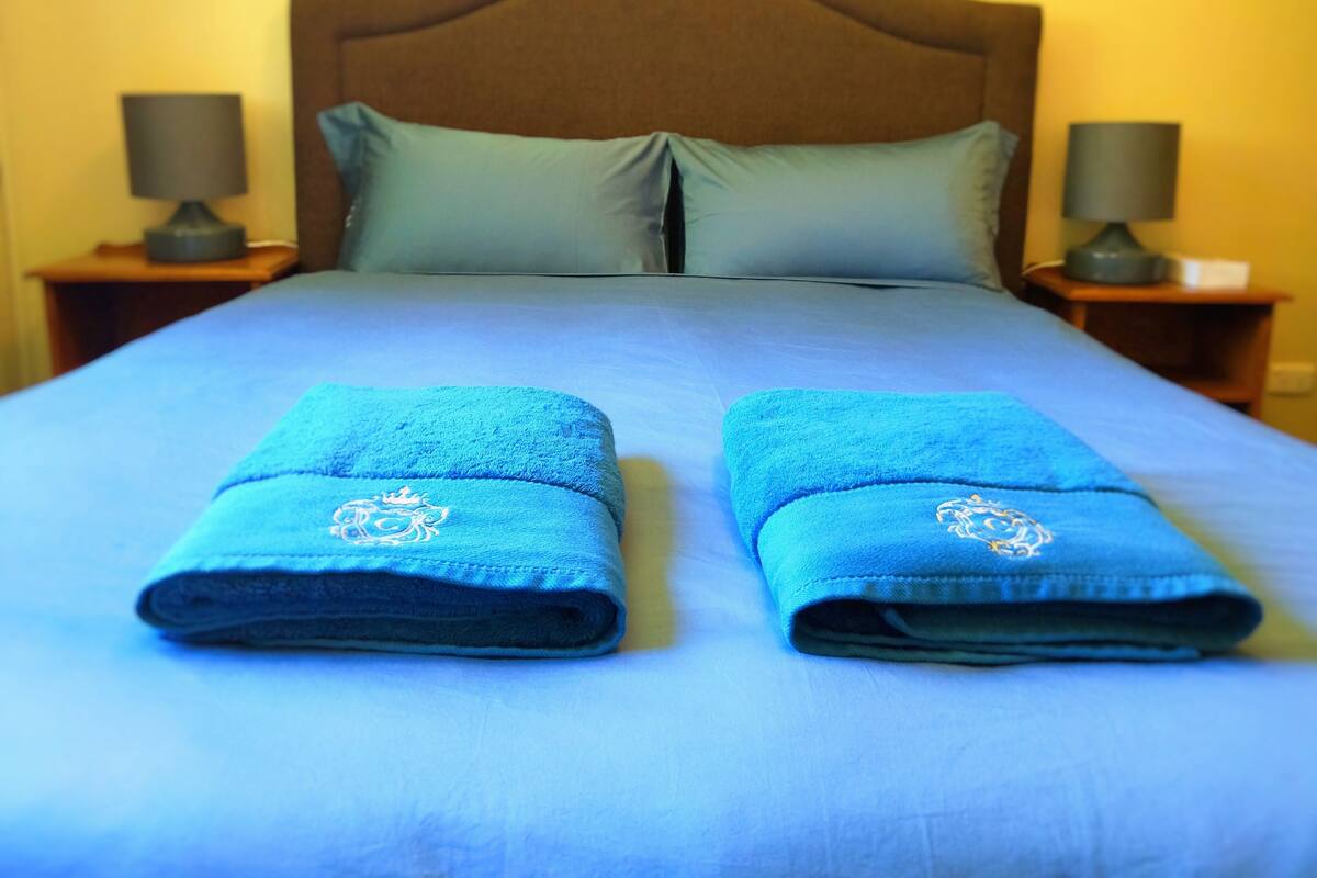 Una cama bien hecha con dos toallas dobladas y un cabecero de madera.
