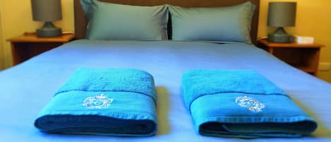 Ein ordentlich bezogenes Bett mit zwei gefalteten Handtüchern und einem hölzernen Kopfteil.