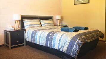 A neatly made bed with striped bedding, two bedside lamps, a small bedside table with a tissue box, and a framed picture on the wall.