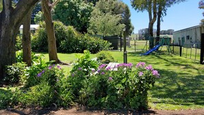 A park with a playground, including a slide, surrounded by trees and flowering plants. - Twelve Apostles Motel & Country Retreat (Princetown)