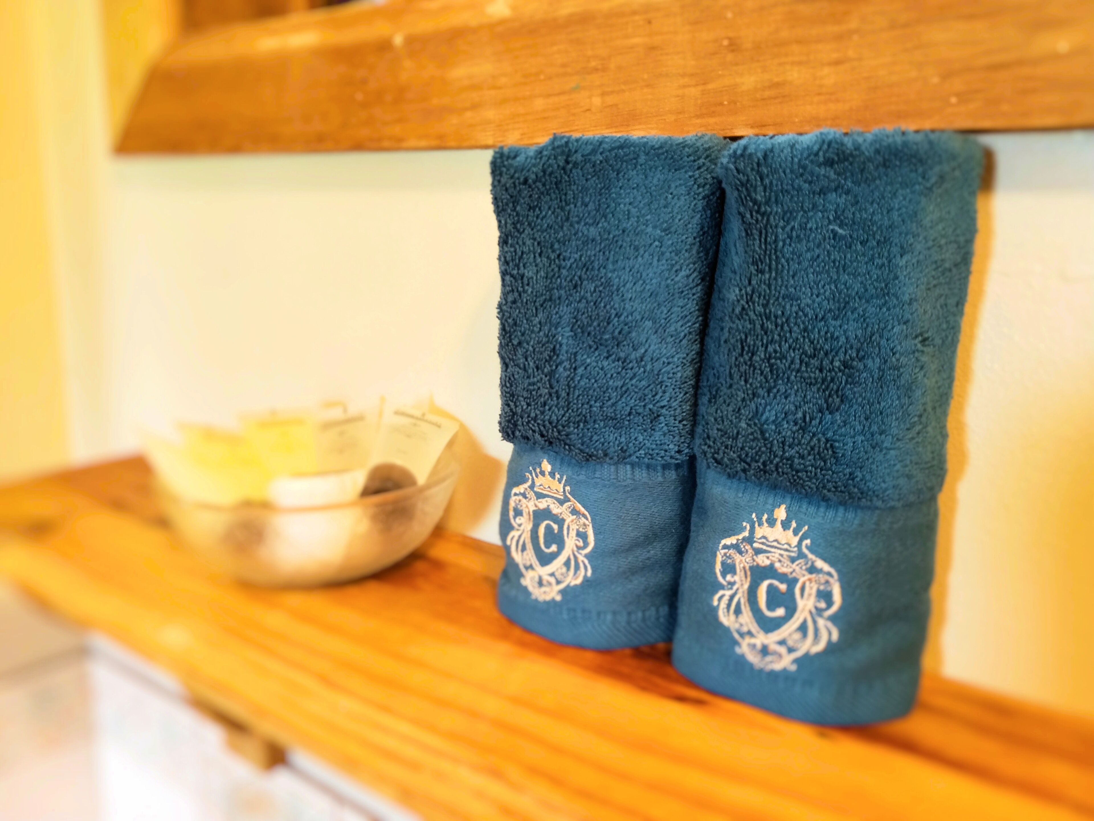 A pair of blue towels with embroidered monograms on a wooden surface next to a bowl.