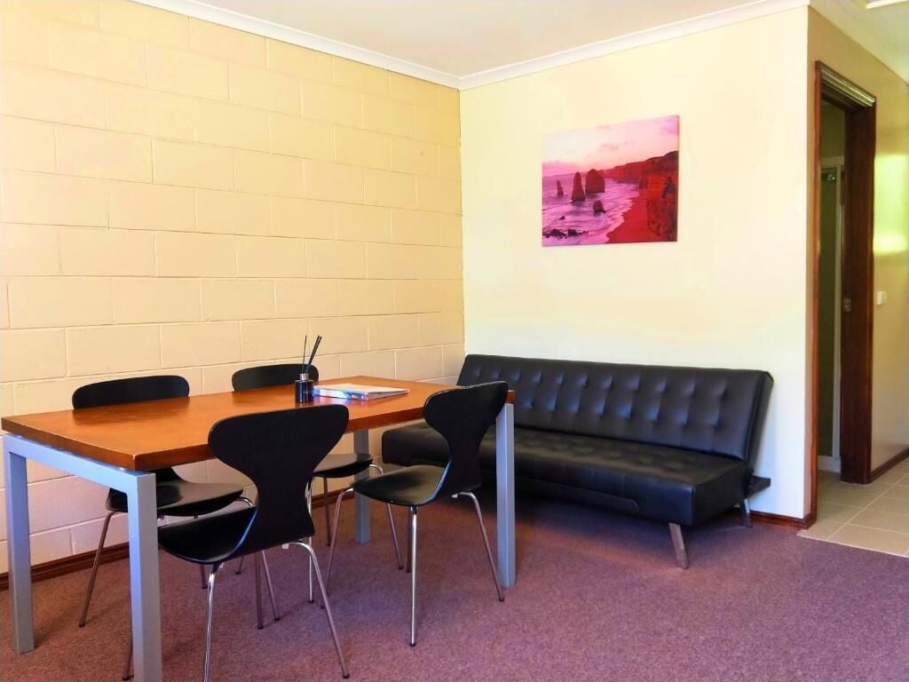 A room with a wooden table, four black chairs, a black sofa, and a painting on the wall.