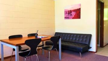 A room with a wooden table, four black chairs, a black sofa, and a painting on the wall.