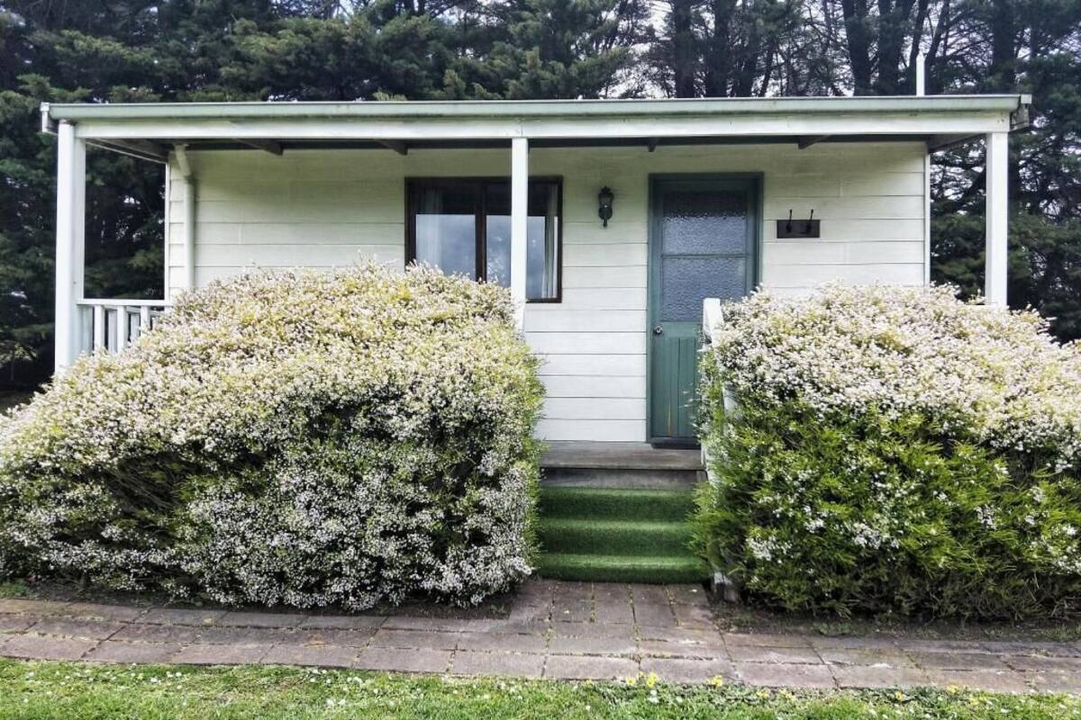 Una casa pequeña de un piso con un porche, una puerta verde y unos escalones que llevan a la entrada.