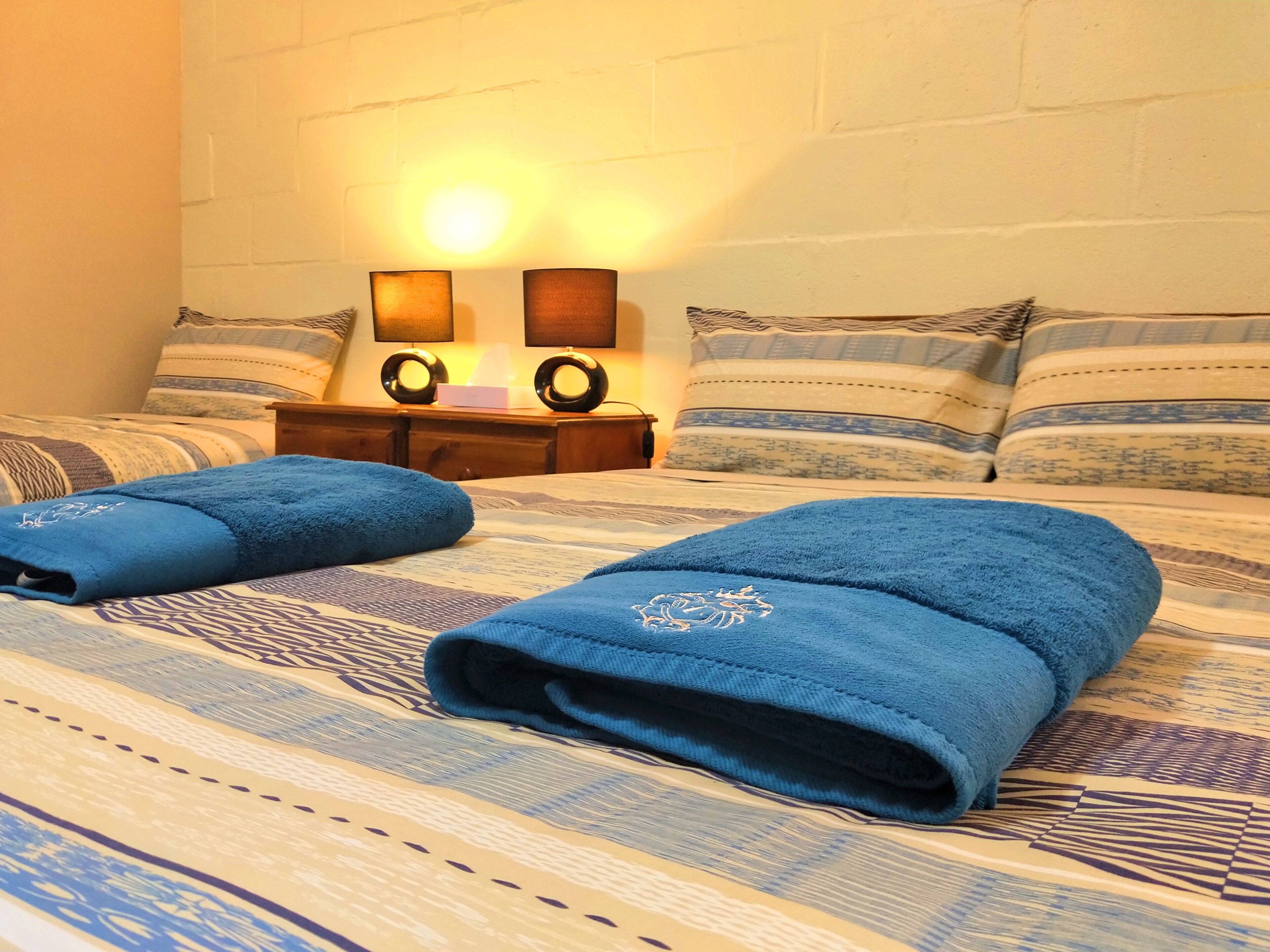 A neatly made bed with blue towels, a wooden nightstand with two lamps, and striped pillows.