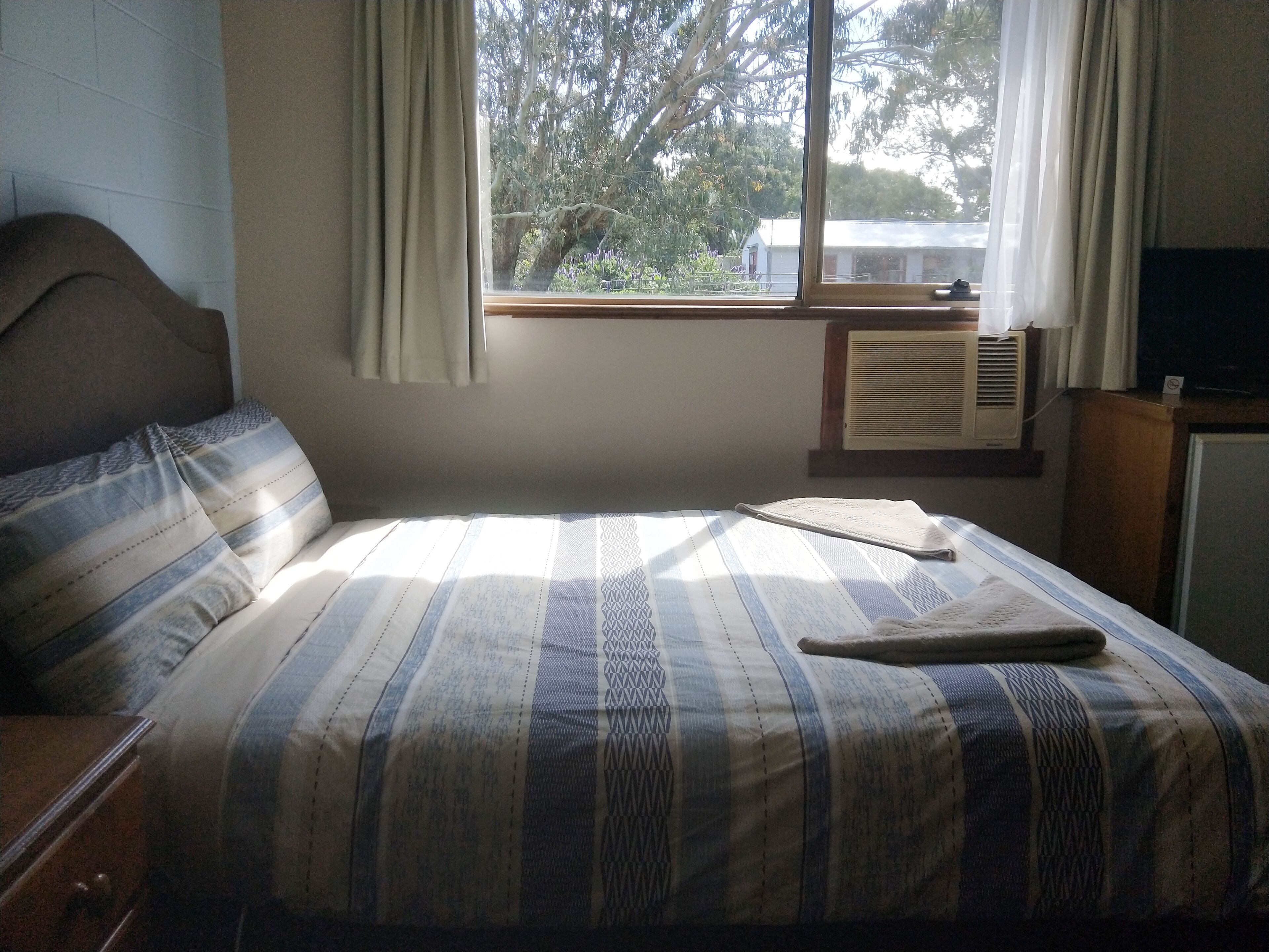 Un dormitorio con cama, ventana con cortinas, radiador y televisor.