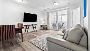 A modern living room with a flat-screen TV, a sofa, a dining table, and a ceiling fan. - Cairns Central Plaza Apartment Hotel (Cairns)