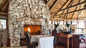 Una chimenea de piedra con fuego, una mesa de comedor con sillas y un banco de madera.