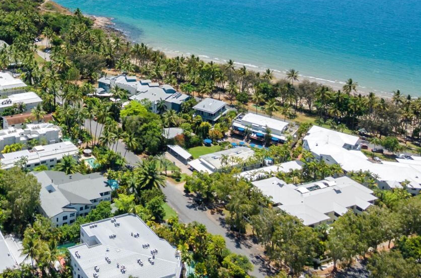 An aerial view of a coastal hotel with multiple buildings, a beach, and palm trees.