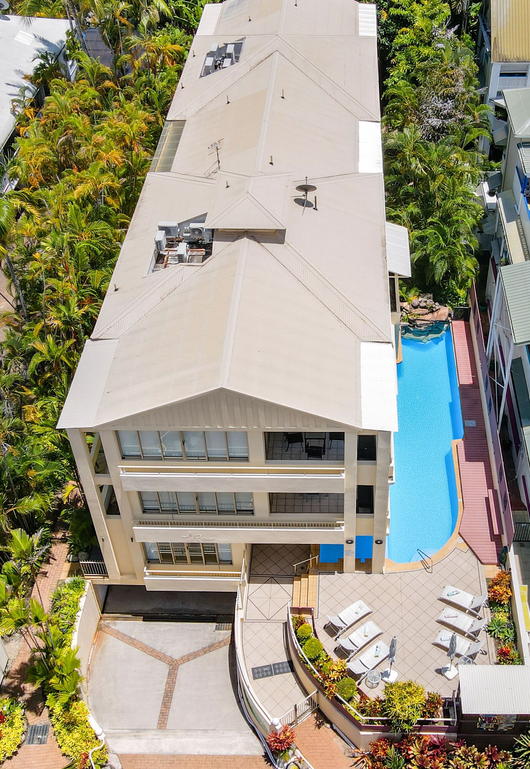 Ein mehrstöckiges Hotel mit Pool auf dem Dach, Sitzgelegenheiten im Freien und üppiger Bepflanzung rund um das Anwesen.