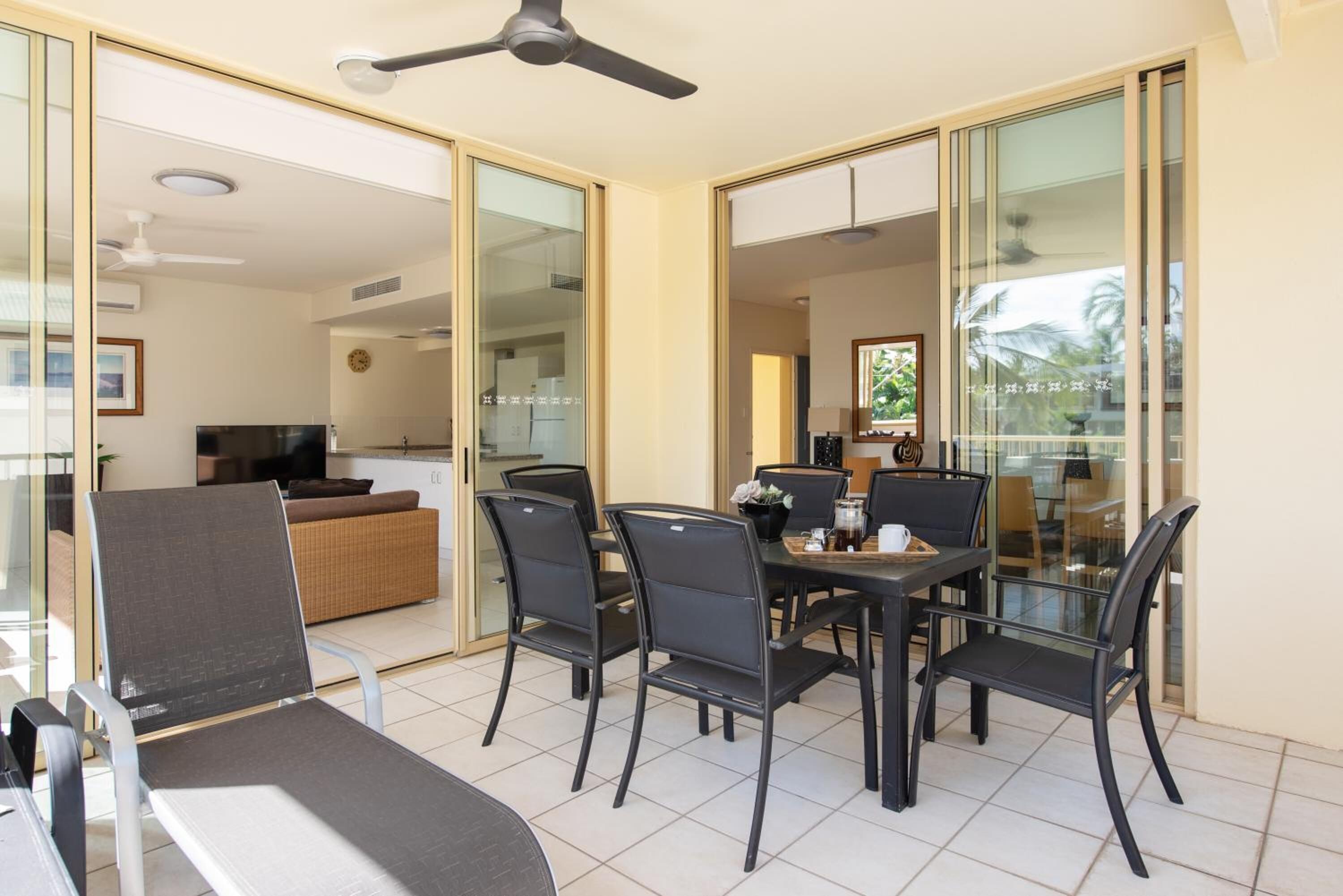A dining area with a table and chairs, a ceiling fan, and a kitchen in the background.