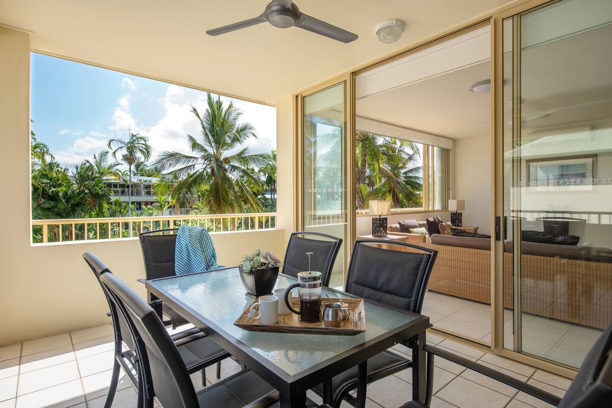 A balcony with a table set for two, a coffee maker, and a tray with cups and a pot.