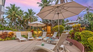 A patio area with wicker lounge chairs, a small table, and umbrellas. - Silkari Reflections of Port Douglas (Port Douglas)