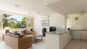 A modern living room with a sofa, coffee table, and a kitchen area with a dishwasher. - Silkari Reflections of Port Douglas (Port Douglas)