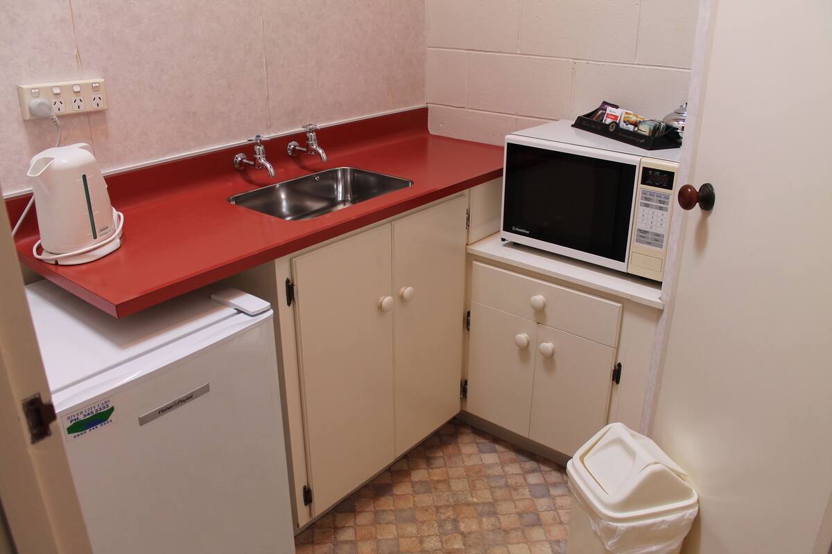 Uma cozinha compacta com bancada vermelha, micro-ondas branco, pia e uma geladeira pequena.