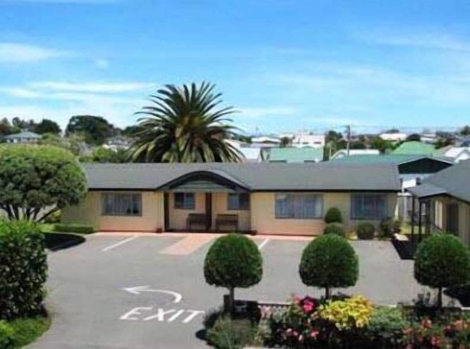 A building with a parking lot marked with an 'EXIT' sign, surrounded by greenery and other buildings.