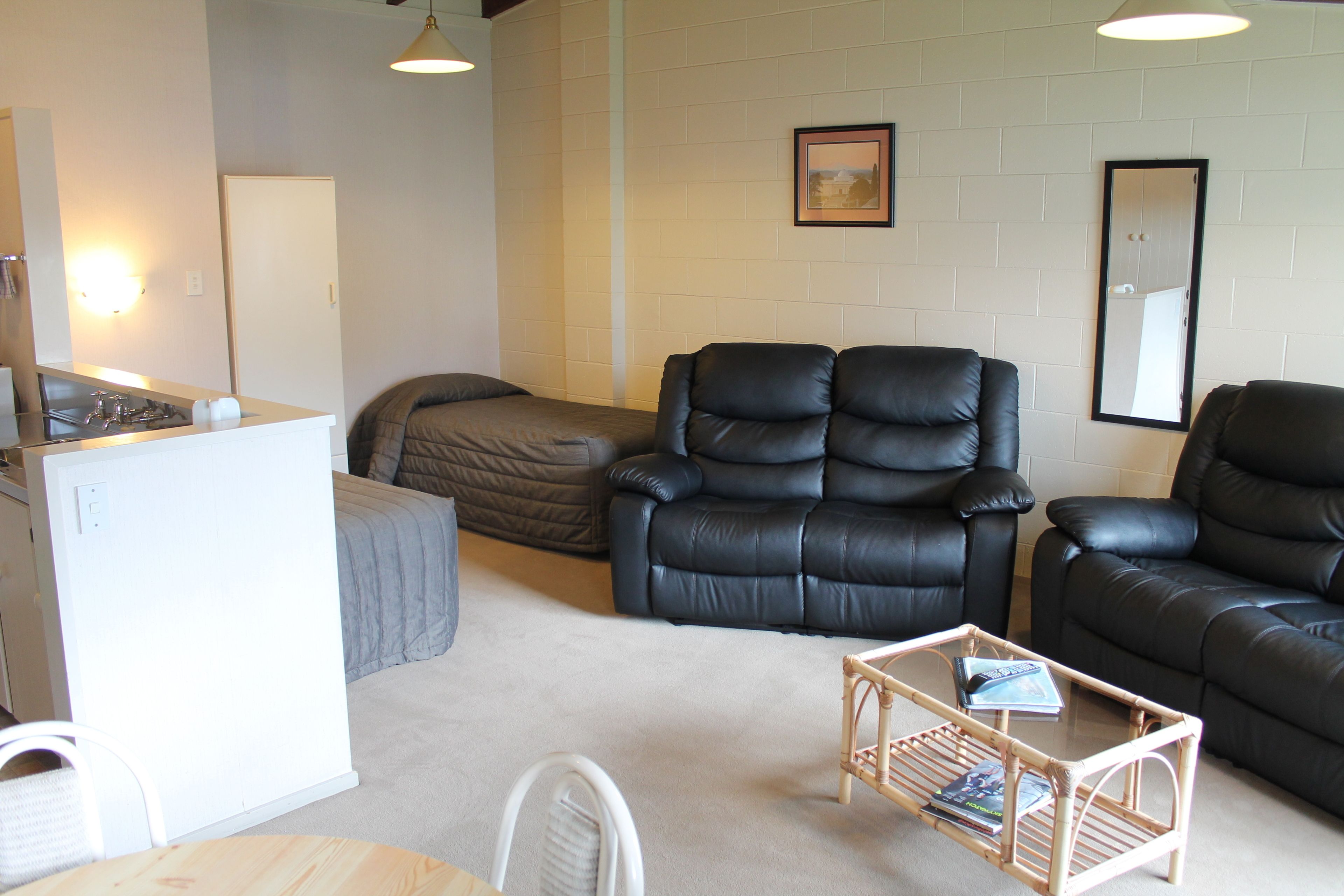 A compact living space with a kitchenette, a sofa, a chair, and a small table.