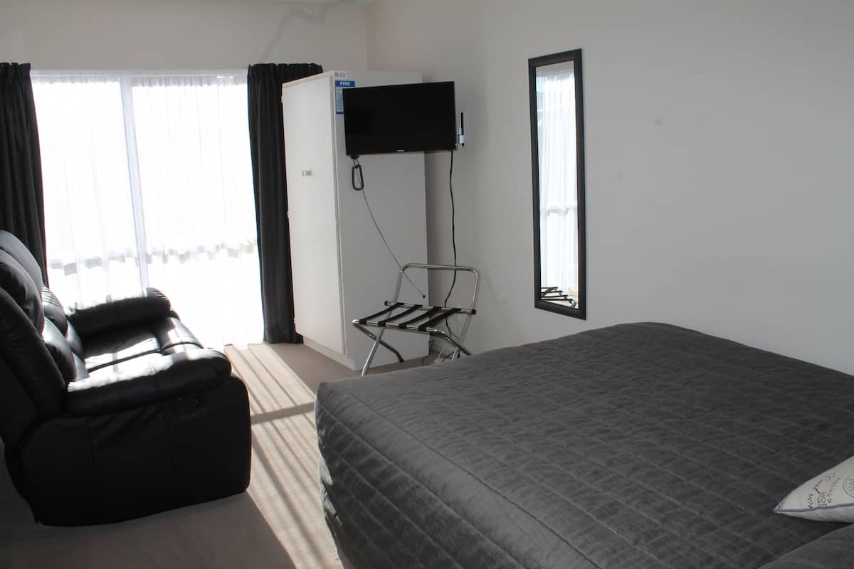 Quarto com cama, cadeira, TV fixada na parede e janela com cortinas.