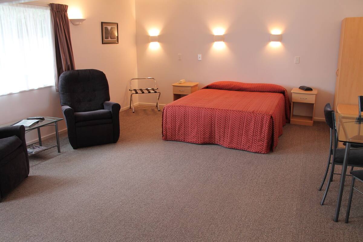 Quarto de hotel com cama, cadeira, escrivaninha e abajur.