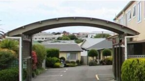 Una calle residencial con entrada porticada, casas y cielo despejado.