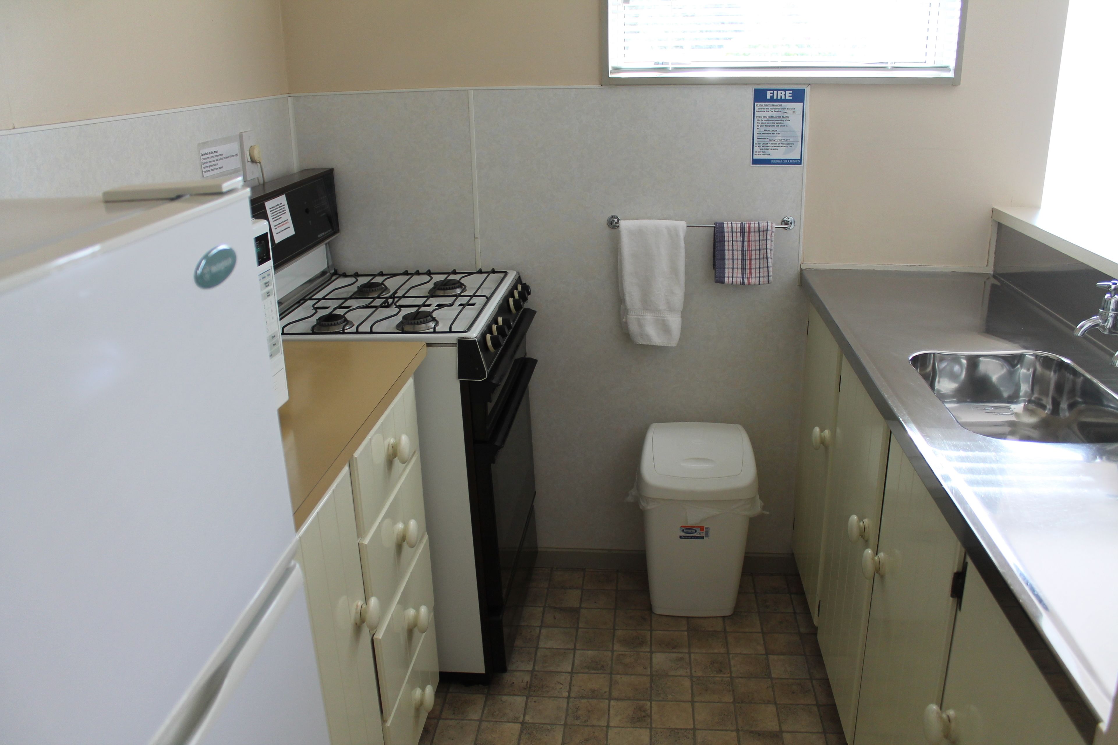A compact kitchen with a gas stove, a sink, and a trash bin.