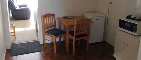 A small kitchenette with a refrigerator, microwave, and a wooden table with two chairs.