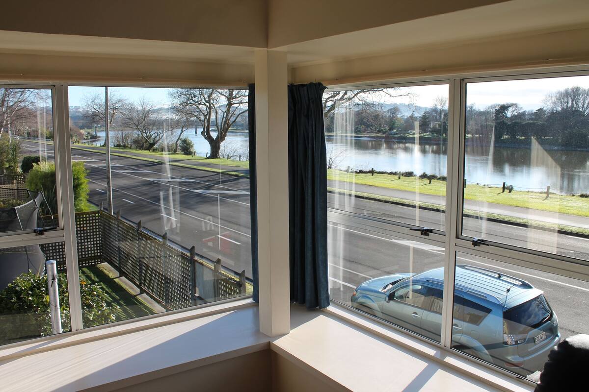 Quarto com uma grande janela com vista para um parque de estacionamento e um corpo de água.