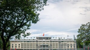 A large building with a flag on top, surrounded by a fence and greenery. - Happy Life Hotel (Ho Chi Minh City)