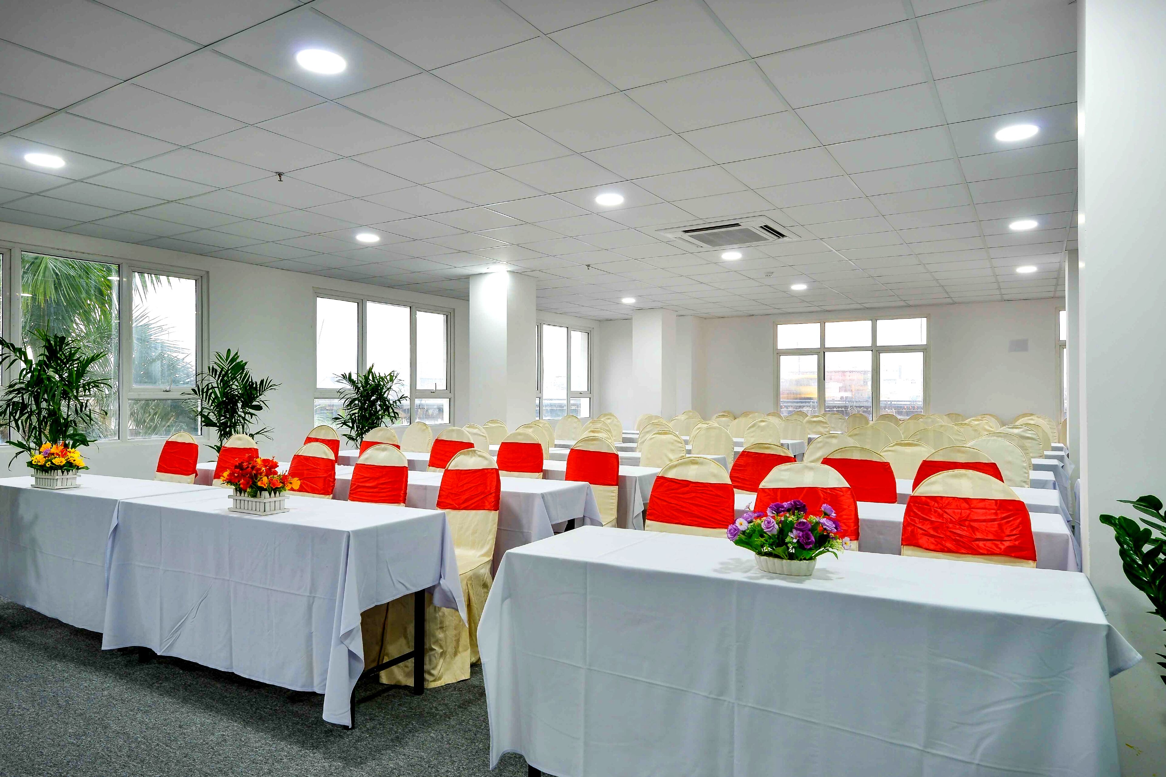 A conference room with multiple tables, each with a white tablecloth and red and white chair sashes.