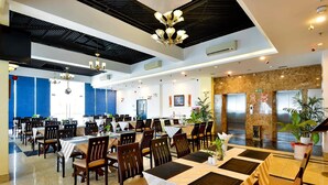 A spacious dining area with multiple tables and chairs, ceiling fans, and decorative lighting fixtures. - Happy Life Hotel (Ho Chi Minh City)