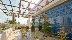 A rooftop terrace with a glass enclosure, potted plants, and outdoor furniture. - Happy Life Hotel (Ho Chi Minh City)