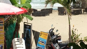 A beachside setting with a red umbrella, a signboard, and a parked motorcycle. - Otres Beach Resort (Sihanoukville)