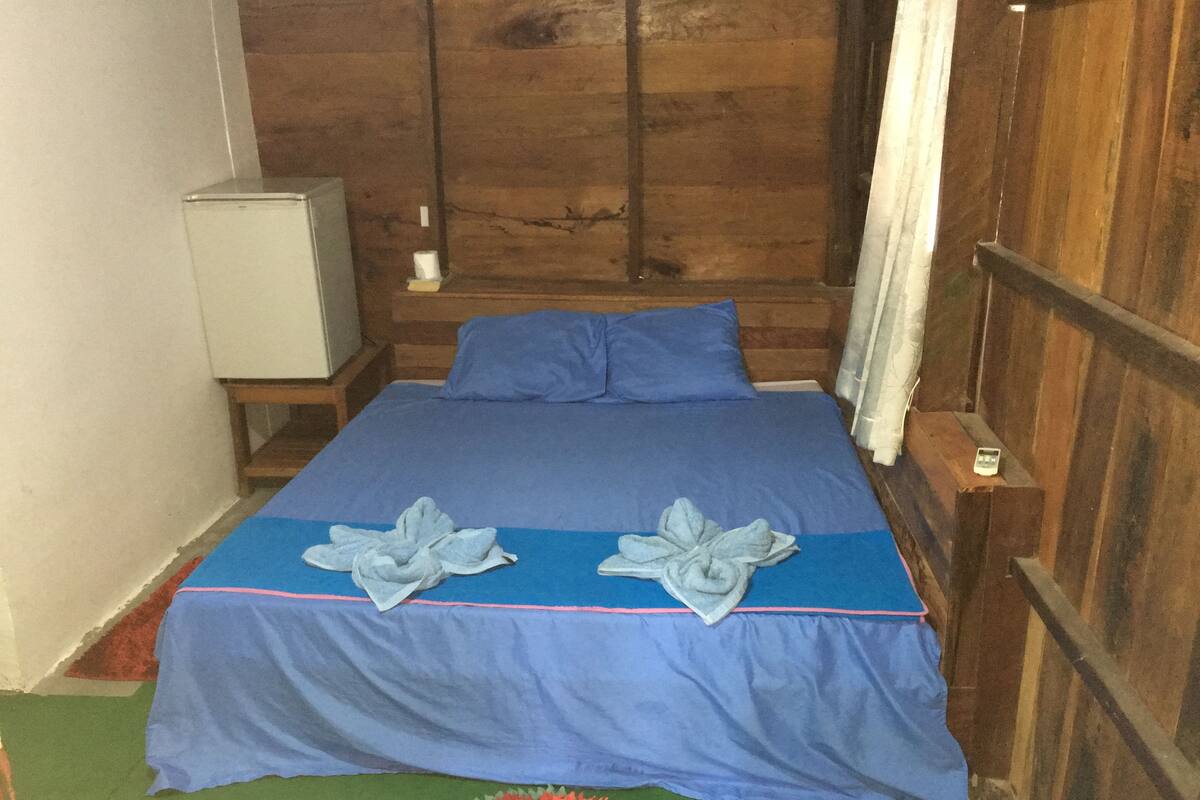 Un lit avec une couvre-lit bleue et des oreillers, une tête de lit en bois, une petite table de chevet avec une lampe et un tapis vert.