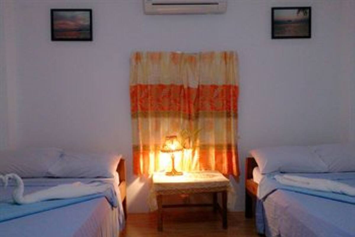 Une chambre avec deux lits simples, une petite table avec une lampe et un rideau.