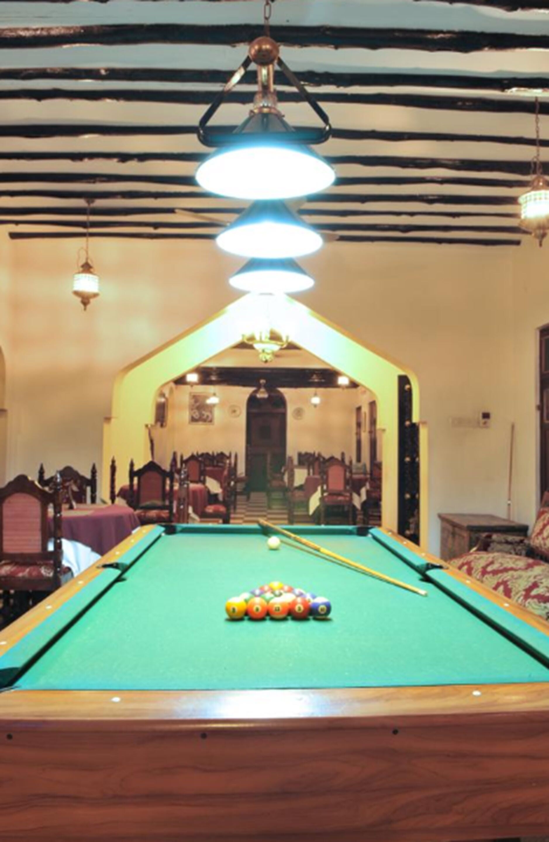 A pool table with balls in a room with wooden beams on the ceiling and a chandelier.