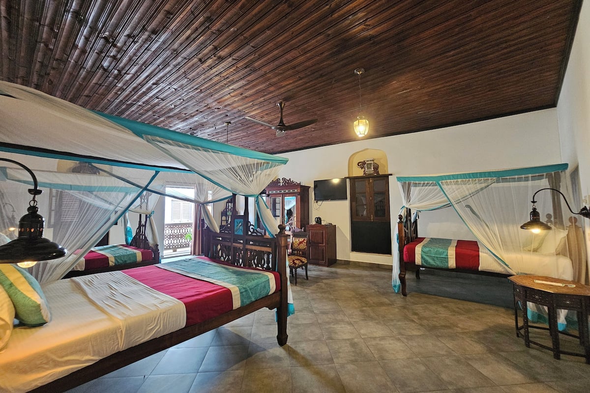 A room with two beds, each with a mosquito net, wooden headboard, and bedside lamps.