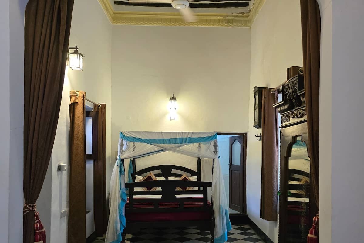 A room with a checkered floor, a bed with a canopy, a ceiling fan, and a wall-mounted light fixture.