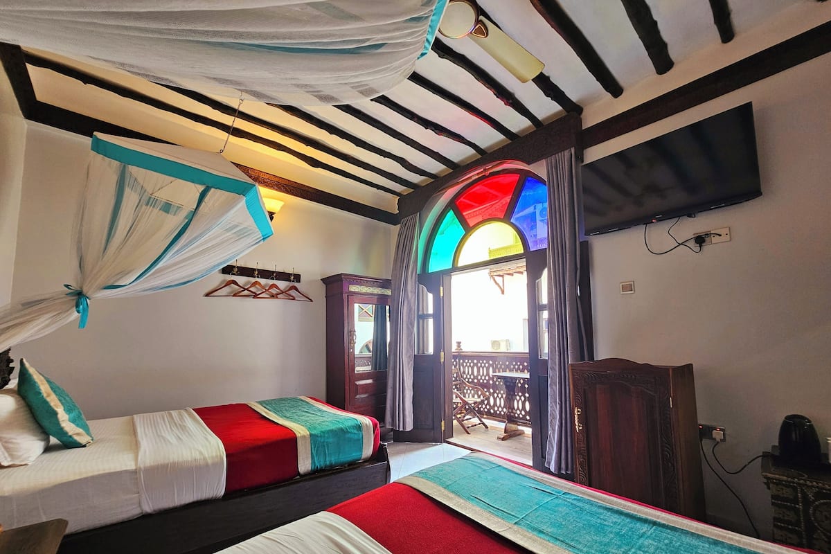 A room with two beds, a TV, a wardrobe, and a window with colorful stained glass.